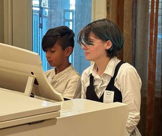A child and a teacher sitting playing the piano together.